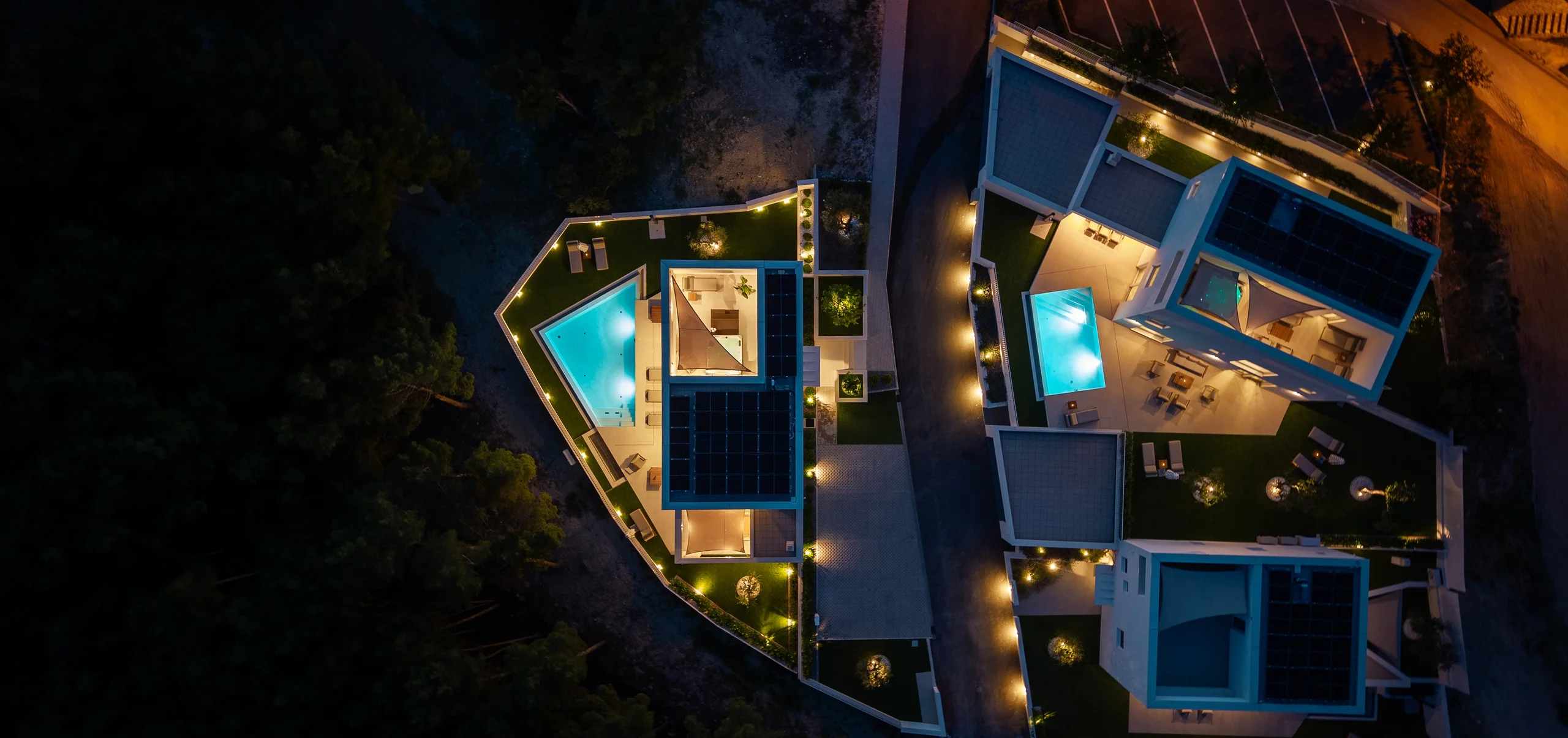 Aerial night view of ABC Villas with illuminated pools and rooftop terraces.